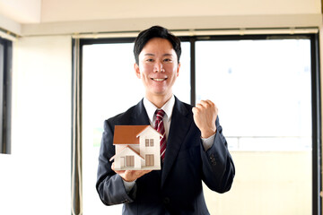 住宅模型を持ちガッツポーズをするスーツ姿の男性のビジネスパーソン