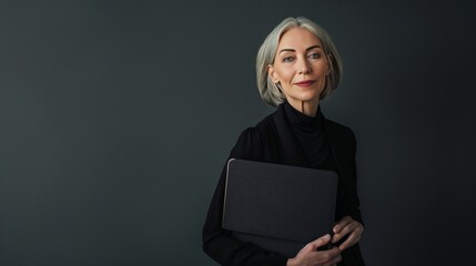 Elegant and confident mature woman leader holding laptop and smiling on dark grey background