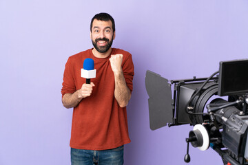 Reporter man holding a microphone and reporting news over isolated purple background celebrating a victory in winner position