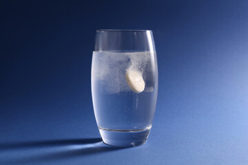 Effervescent pill dissolving in glass of water on blue background