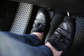 Man in black shoes pushing on pedal of car brake, closeup