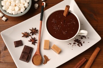 Tasty melted chocolate in cup, marshmallows, candies and spices on wooden table, flat lay