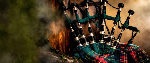Several bagpipes standing upright, leaning against a wooden surface, with a green and red tartan draped over them
