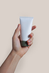 Female hand holding white tube of face and body cream mockup on light color isolated background. Concept of beauty products and branding