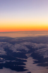 View out of an airplane window of a snow-covered mountain range at sunset