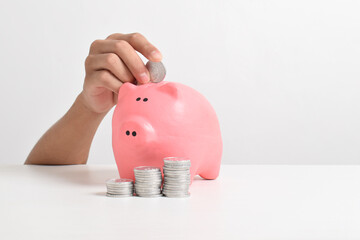 Hand putting coins into piggy bank isolated on white background. Business finance, savings and...