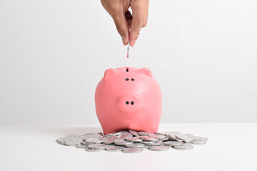 Hand putting coins into piggy bank isolated on white background with copy space. Saving, investment...
