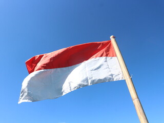 The red and white flag of the Republic of Indonesia is attached to a bamboo stick.