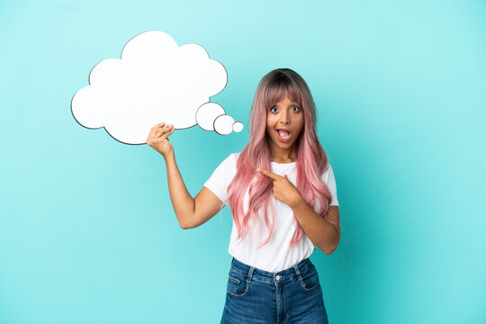 Young mixed race woman with pink hair isolated on blue background holding a thinking speech bubble with surprised expression