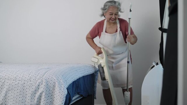 Handheld shot Footage: A housekeeper in an apron vacuums a bedroom, visibly tired. This effort guarantees the area remains clean and well-kept.