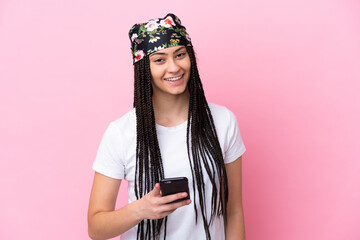 Teenager girl with braids over isolated pink background using mobile phone