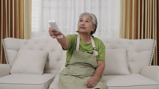 Handheld Shot Footage, A fatigued housekeeper in an apron cleans the house. Overheated, she switches on the air conditioning to cool off in the living room.