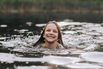 Fototapeta premium Beautiful little girl, happy child swims in water on lake, sea during summer holidays. Photography, portrait.