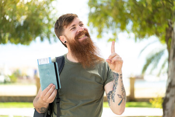 Redhead man with beard holding a passport at outdoors intending to realizes the solution while lifting a finger up