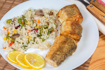 Serving of fried hake hubbsi pieces with rice and vegetables