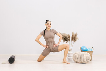 Fototapeta premium An athletic woman in sportswear is doing a workout to stretch her body and develop her muscles. Active girl doing fitness or yoga in home gym. Healthy body and sportswear concept.