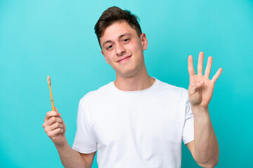 Fototapeta premium Young Brazilian man brushing teeth isolated on blue background happy and counting four with fingers