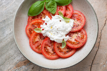 Beige plate with sliced tomatoes and stracciatella or stretched curd fresh cheese, horizontal shot, middle close-up, elevated view