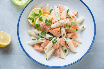 Blue and white plate with creamy salmon pasta, horizontal shot on a grey granite surface, middle close-up