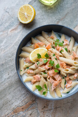 Bowl of penne pasta with salmon flakes on a grey and roseate granite background, high angle view, vertical shot