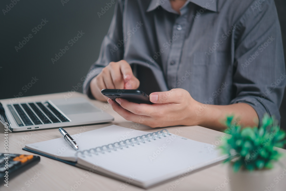 Poster professional using smartphone at desk with laptop and notebook, representing modern business communi