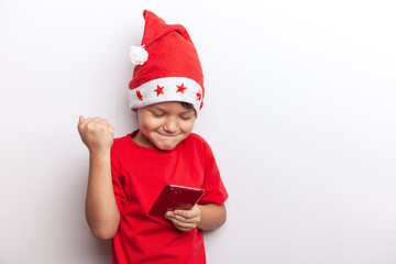 a boy in a Santa costume holds a smartphone in his hands. an emotional little santa. a cheerful child for Christmas with a phone.