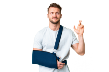 Young caucasian man with broken arm and wearing a sling over isolated chroma key background with fingers crossing and wishing the best