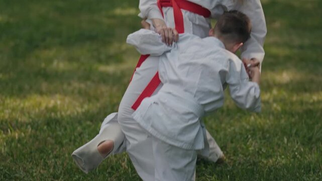 A mother and son are practicing karate in the park. The mother is teaching her son some basic self-defense moves. They are both wearing white karate uniforms.