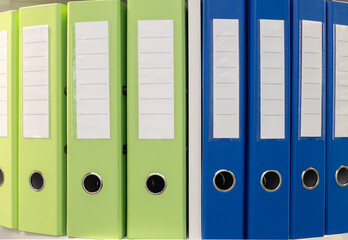 A row of green and blue binders are lined up on a shelf