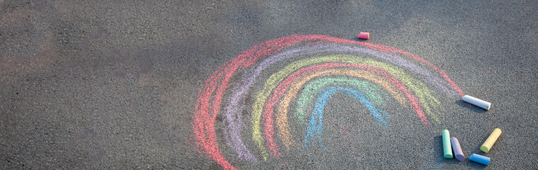 Sidewalk chalk drawing. A rainbow painted on the asphalt. Kids activities. Colored chalks background. Back to school playground copy space.