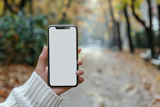 A mobile phone held in woman’s hand, with the screen facing the viewer and displaying a blank white screen