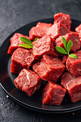 Fresh, raw beef cubes neatly arranged on a black plate, garnished with a sprig of green leaves, perfect for gourmet cooking and food graphy.