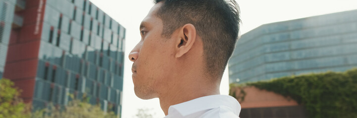 Fototapeta premium Close-up of young businessman walking down the street on modern buildings background, panorama