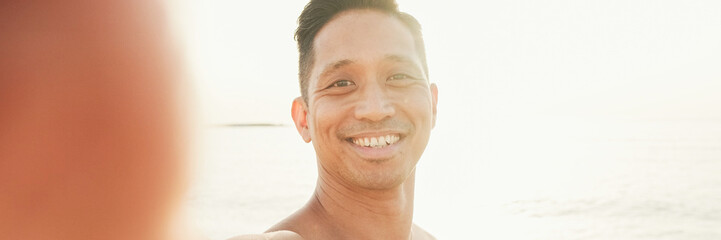 Close up of guy, an athlete with a naked torso standing on the beach makes a selfie on a smartphone, panorama