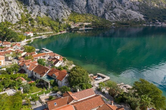 Aerial view of the charming coastal village of Orahovac in Montenegro, with terracotta-roofed houses nestled along the bay, surrounded by lush greenery and crystal-clear turquoise water