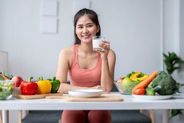 Young woman drinking milk surrounded by fresh fruits and vegetables