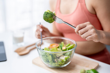 Young sporty woman eating healthy salad at home after workout