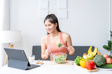 Young asian woman eating salad and following recipe on digital tablet at home
