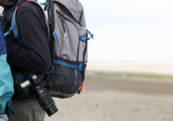 A traveler is wearing a backpack with straps and carrying a camera in nature.