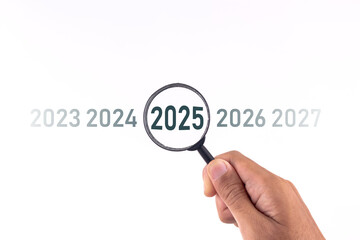 Hand holding a magnifying glass to looking at the word year 2025 on white background. Business plan target strategy, goals, and trends in 2025