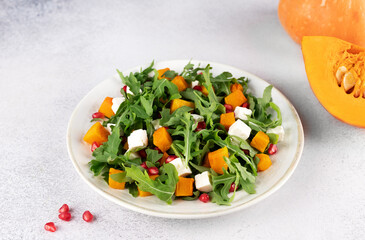 Pumpkin salad with arugula, feta cheese and pomegranate seeds on a gray background. Top view. Thanksgiving Dishes.