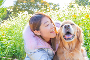 コスモス畑で笑い合っているゴールデンレトリバーと若い日本人女性