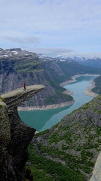 two individuals at the edge of a cliff, gazing at a lovely lake. The backdrop adds a mysterious touch to the enchanting scene, a couple of men and women hiking the Trolltunga, Norway