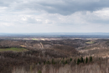 Hilly countryside during cloudy day, village with scattered houses and hills overgrown with leafless forest in March