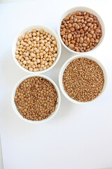Four white bowls standing on white background, each containing different legume