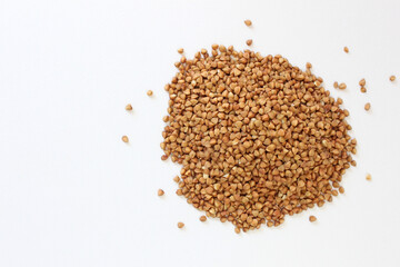 Pile of uncooked buckwheat groats is lying on a white background, creating a textured and wholesome food image