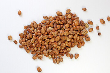 Variety of pinto beans scattered on a white background, creating a rich brown pattern perfect for food projects. Organic and uncooked, they highlight plant-based protein and fiber