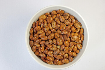 White bowl is overflowing with pinto beans, captured from a high angle against a clean white backdrop