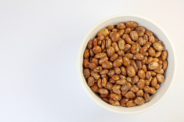 White bowl is overflowing with pinto beans on a white background, perfect for showcasing healthy eating