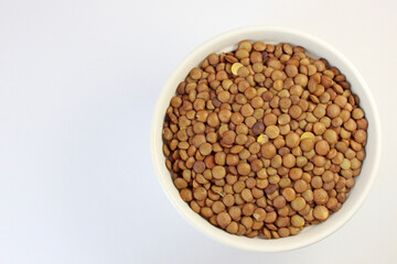 White bowl overflows with brown lentils on a clean background, showcasing their raw, organic goodness. Perfect for vegan diets, high in protein and fiber